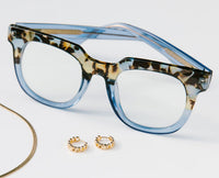 Blue and tortoiseshell glasses with gold hoop earrings on a light gray background