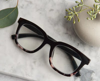 Black eye glasses with marble accents on a marble surface with green leaves