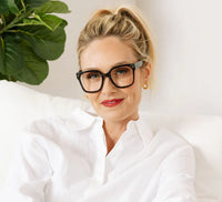 Woman wearing glasses and a white shirt with a plant in the background