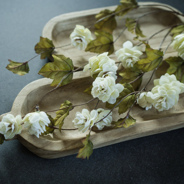 White flowers with green leaves on a wooden tray against a dark background