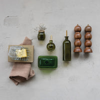 Collection of kitchen items including a green bottle, wooden salt and pepper shakers, and a pink towel on a light gray surface.