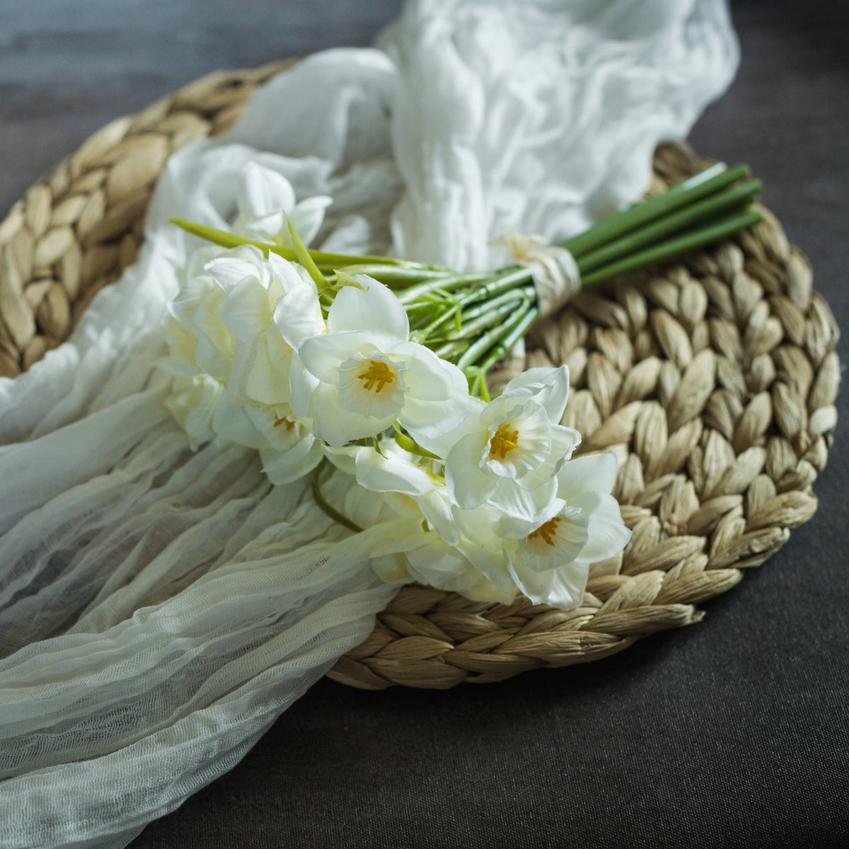 Bouquet of white daffodils on a woven mat with sheer fabric