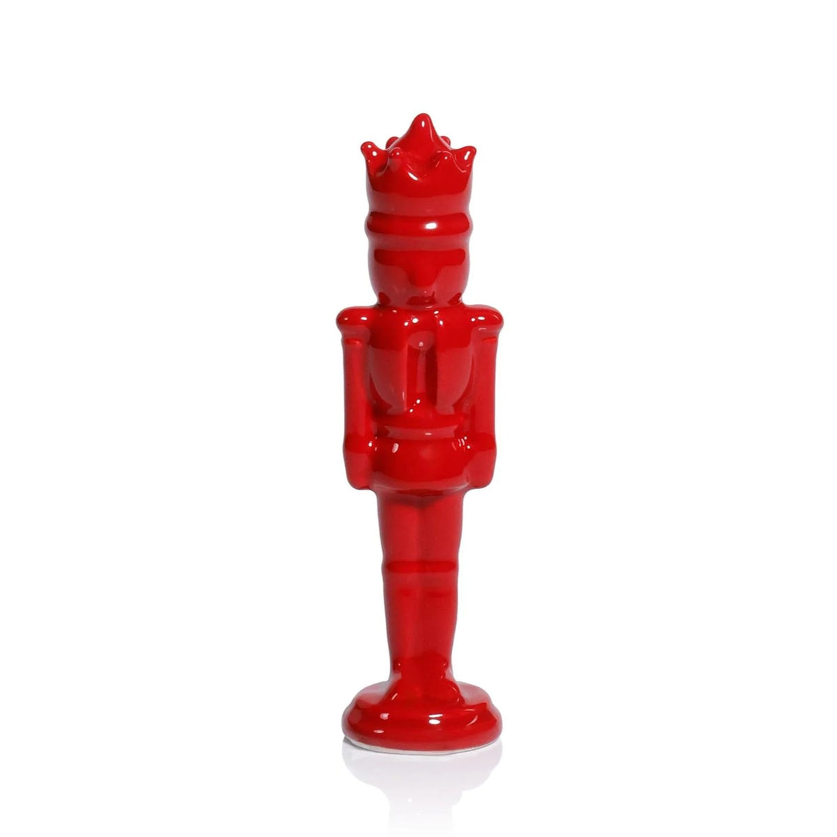 A glossy red ceramic nutcracker figurine with a crown, standing upright on a white reflective surface.