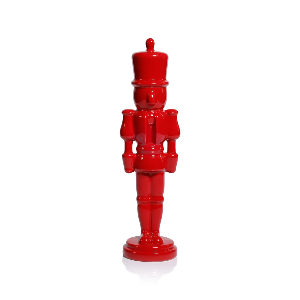 A glossy red nutcracker figurine standing upright on a white reflective surface against a white background.