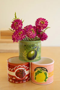 Three ceramic vases painted to imitate old cans with floral arrangements on a wooden surface.