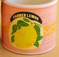 A close-up of a ceramic vase with a retro 'Canned Lemon' design, featuring a yellow lemon illustration on a pink and orange background.