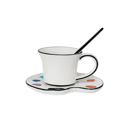White mug with black rim on a matching saucer with color swatches, accompanied by a black stirrer.