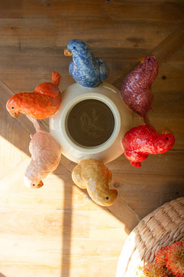 A top down look at a vase that features parrots on the sides, sitting on a wooden surface.