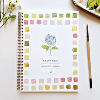 Watercolor workbook titled 'Flowers' by Emily Lex Studio on a white surface with a brush and flowers.