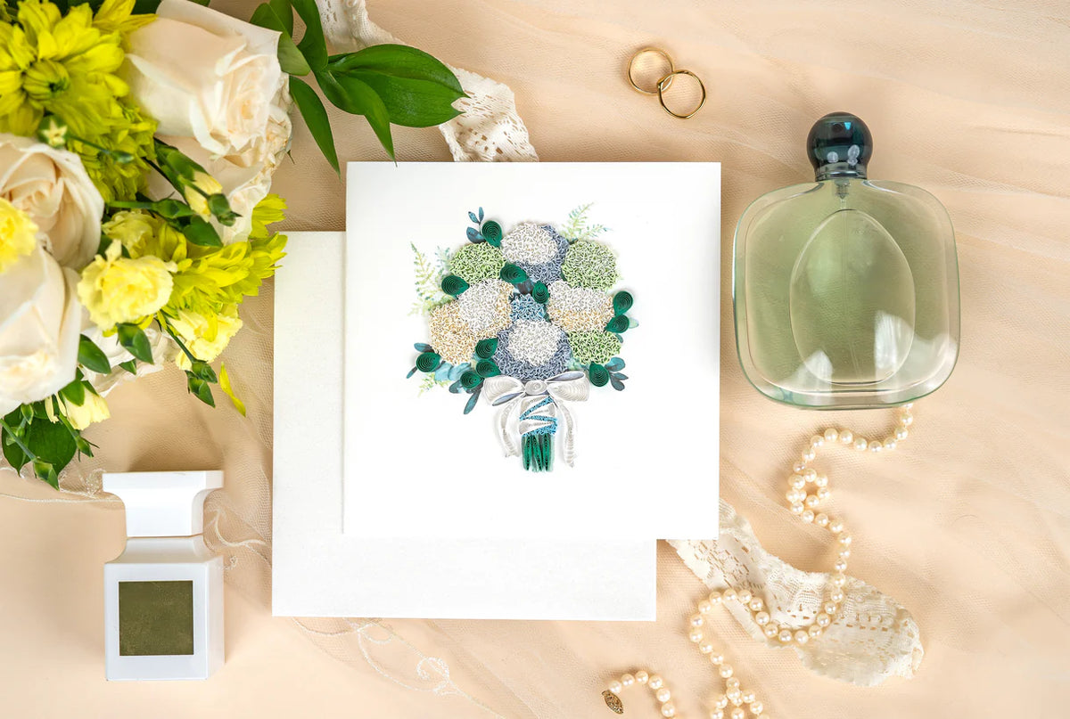 Floral arrangement, card with quilled hydrangea design, and decorative items on a beige surface