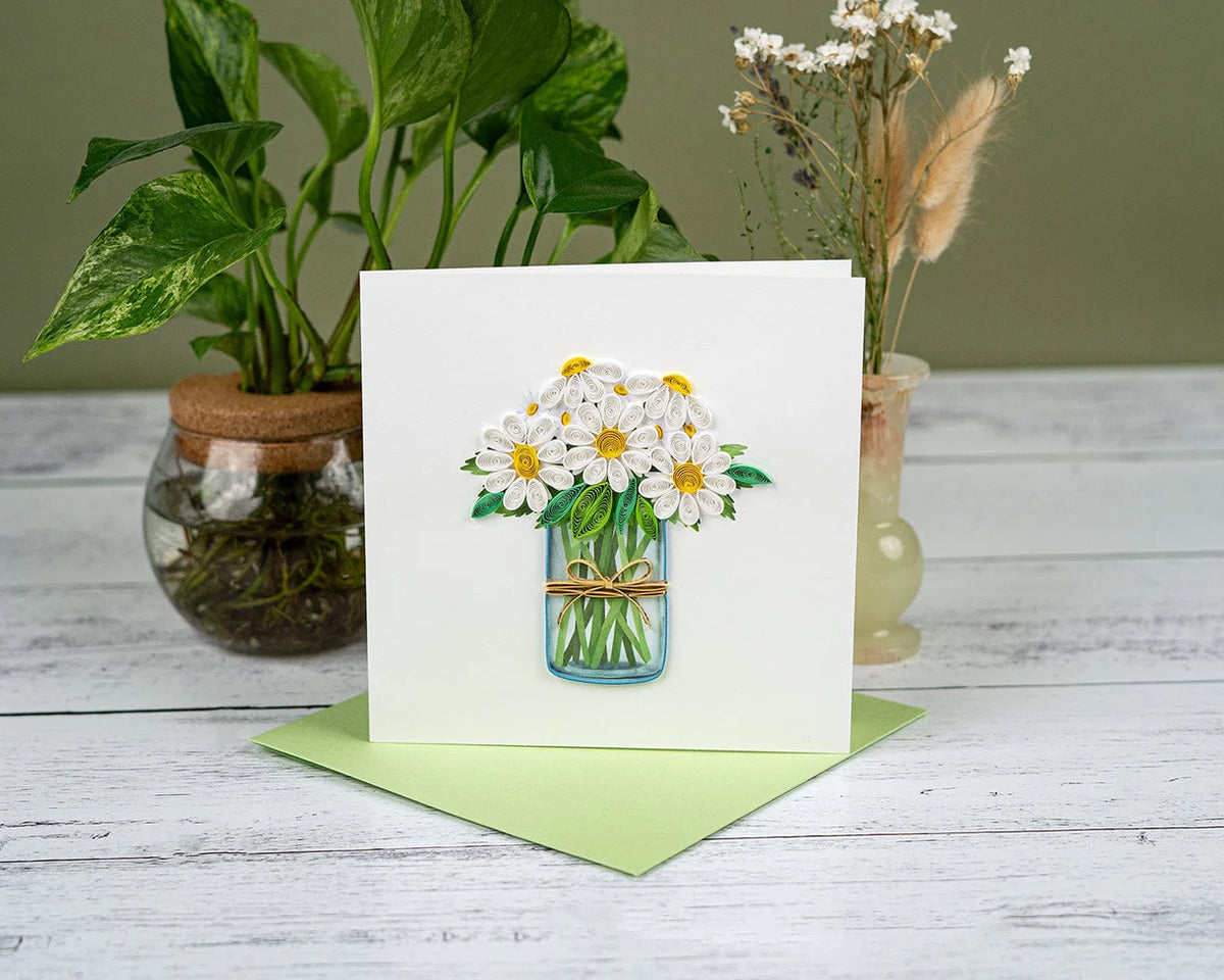 Greeting card with quilled daisy bouquet on a wooden surface with plants in the background