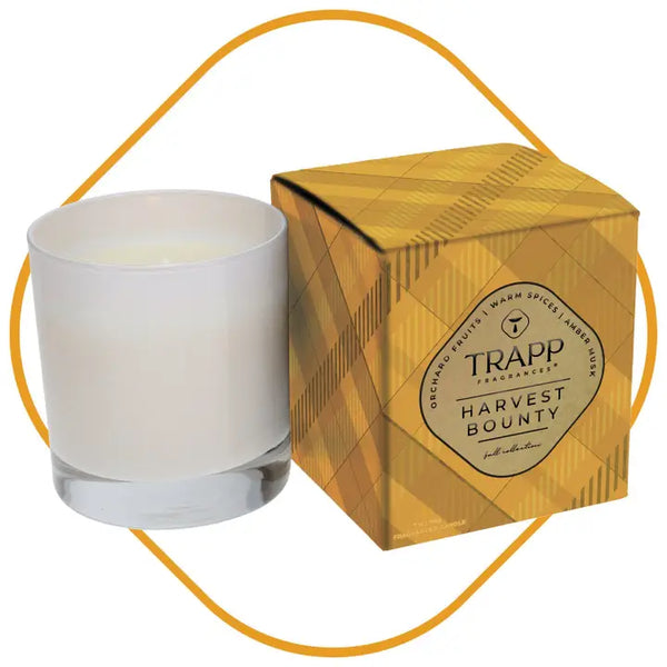 A white glass jar candle next to its gold patterned packaging box, featuring the brand name TRAPP Candle Company and scent name HARVEST BOUNTY.
