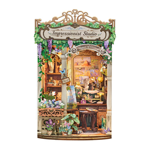 A decorative miniature diy book nook set labeled 'Impressionist Studio' shown against a plain white background. The scene includes a detailed storefront facade with shelves, flowers, plants, lamps, and a central arched window area.
