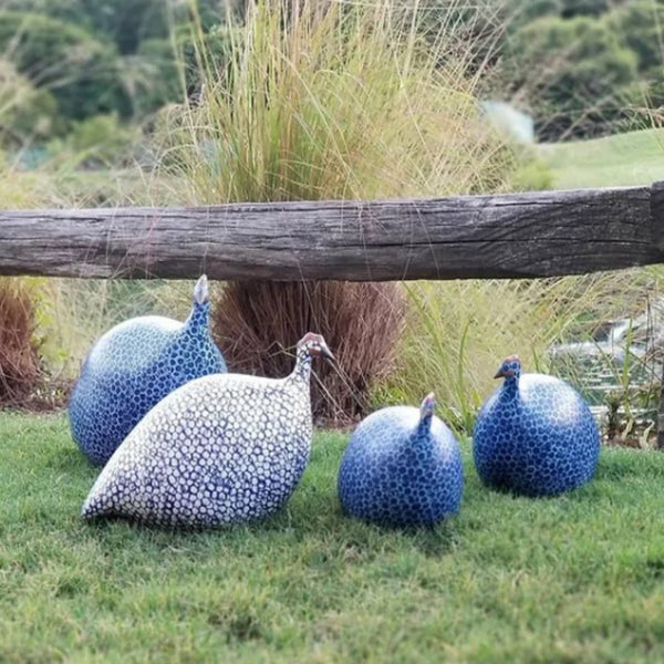 Decorative guinea fowl sculptures on grass with a wooden log and plants in the background