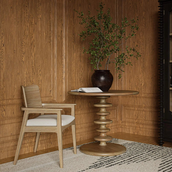 A circular accent table in a room with a plant on book on top of it next to a chair.