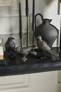 Decorative metal ravens and a vase on a dark surface with a neutral background