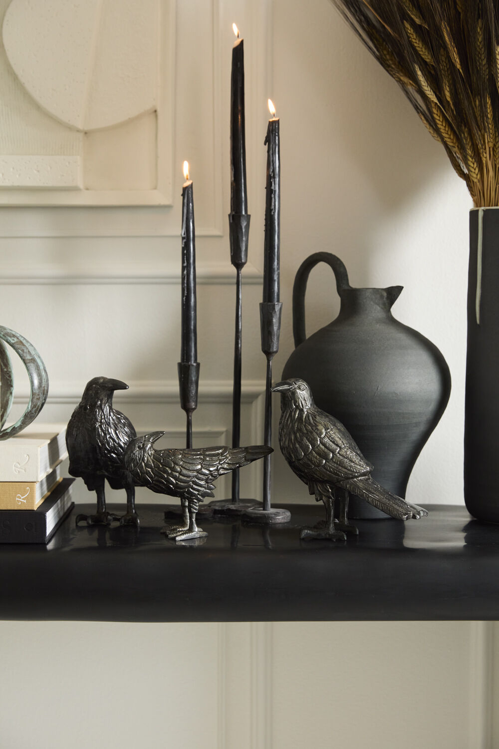 Decorative black raven figure, candles, and vase on a shelf with a neutral background