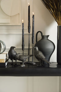 Decorative black raven figure, candles, and vase on a shelf with a neutral background