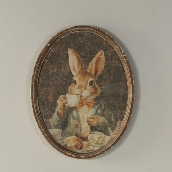 Decorative wall art of a rabbit holding a teacup in an oval frame.