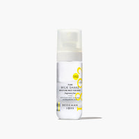 A white pump bottle of Beekman 1802 Pure Milk Shake Moisture Mist for Body, featuring a frosted cap and yellow graphic accents, set against a clean white background with a soft shadow.