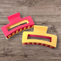 Two colorful hair clips, one red and yellow, the other yellow and red, on a wooden surface.