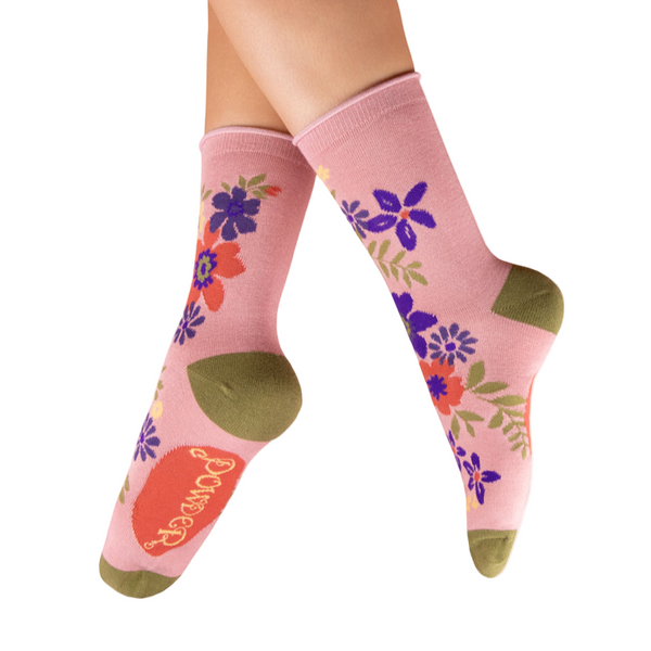 Pink socks with floral designs and green accents worn by a person on a white background