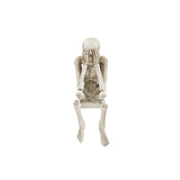 A decorative skeleton shelf sitter with its hands over its mouth in a 'see no evil' pose on a white background.