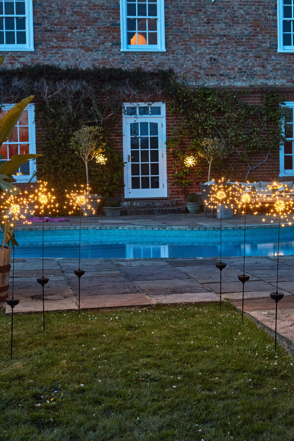 Garden with pool and staked starburst lights in front of a brick building
