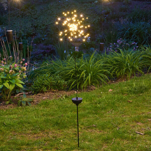 A staked starburst-shaped light in a garden at night.