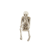 A decorative skeleton shelf sitter with its hands over its mouth in a 'speak no evil' pose on a white background.