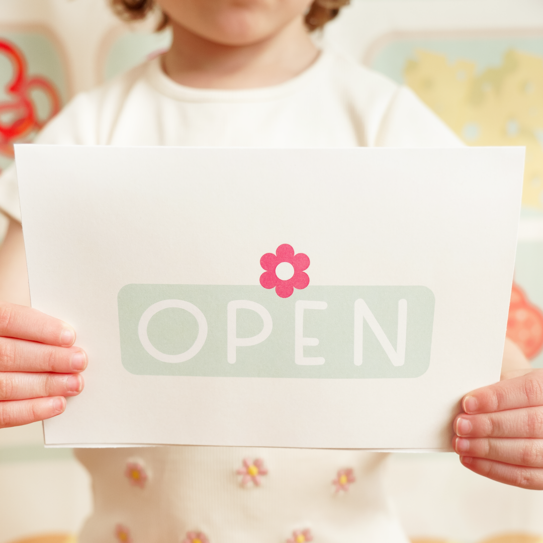 Child holding a sign with 'OPEN' and a flower graphic