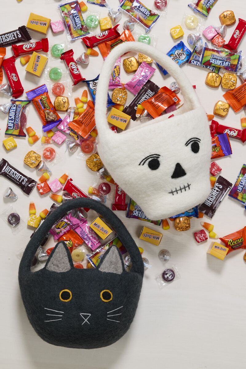 Halloween-themed cat and skull felt baskets filled with candy on a white background.