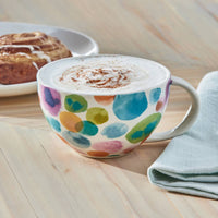Colorful mug with polka dot pattern containing a hot beverage on a wooden surface.